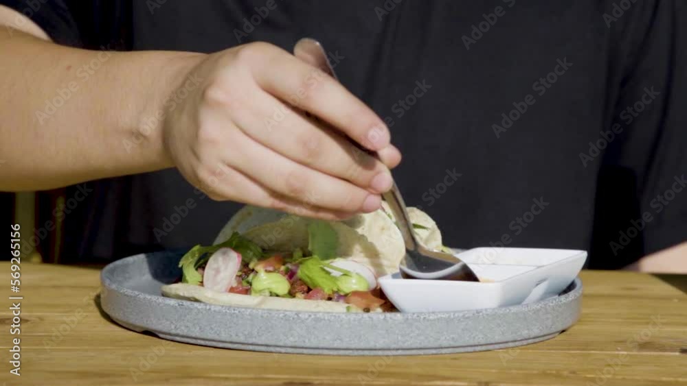 Closeup de persona preparando un Taco de mariscos acompañado de ensalada, queso, y salsas en cámara lenta 