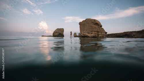 Low angle view of woman paddleboarding through passage between sea rocks