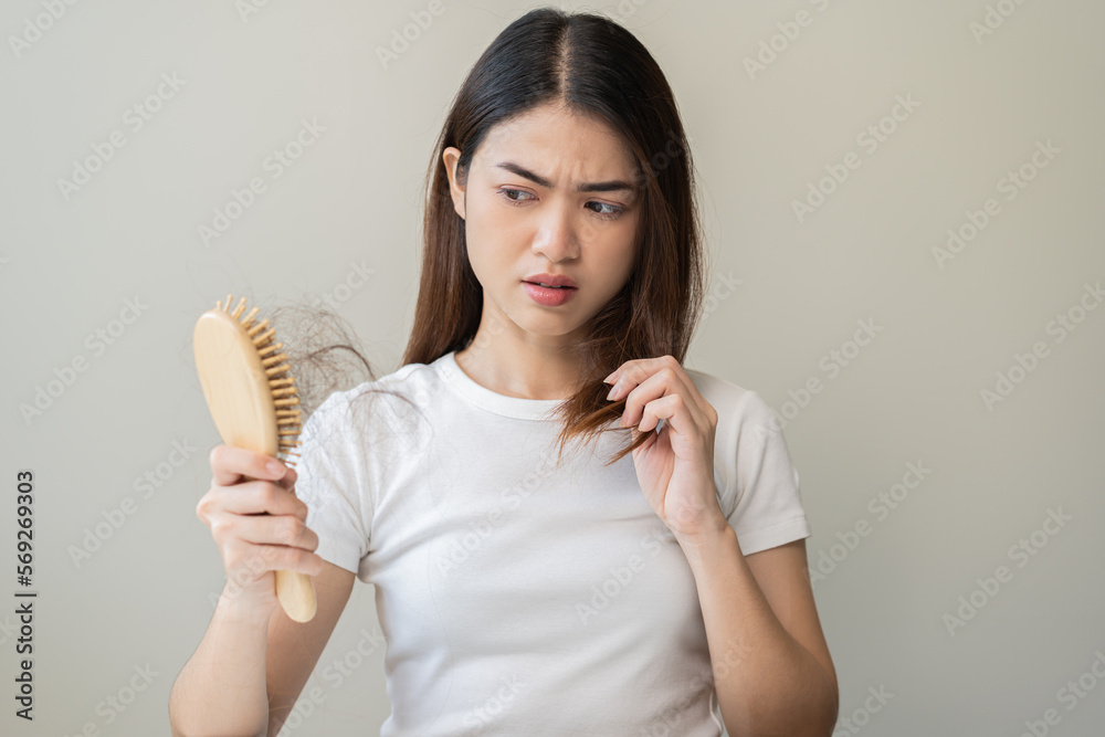 Serious asian young woman holding brush holding comb, hairbrush with fall black hair from scalp after brushing, looking on hand worry about balding. Health care, beauty treatment, hair loss problem. Serious asian young woman holding brush holding comb, hairbrush with fall black hair from scalp after brushing, looking on hand worry about balding. Health care, beauty treatment, hair loss problem.