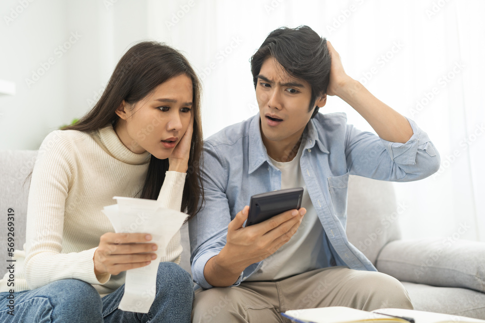 Stressed financial owe asian young couple love hand in holding bills, sitting on sofa together, stressed and confused by calculate expense, mortgage or loan. Debt, bankrupt or bankruptcy people. Stressed financial owe asian young couple love hand in holding bills, sitting on sofa together, stressed and confused by calculate expense, mortgage or loan. Debt, bankrupt or bankruptcy people.