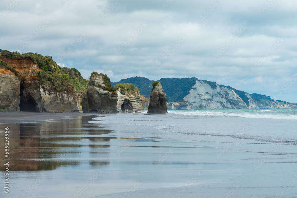 Strand mit schwarzem Sand und Spiegelung und Wellen und Felsen in Neuseeland bei den Three Sisters.