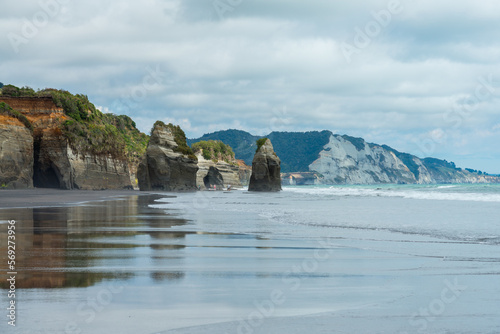 Strand mit schwarzem Sand und Spiegelung und Wellen und Felsen in Neuseeland bei den Three Sisters.