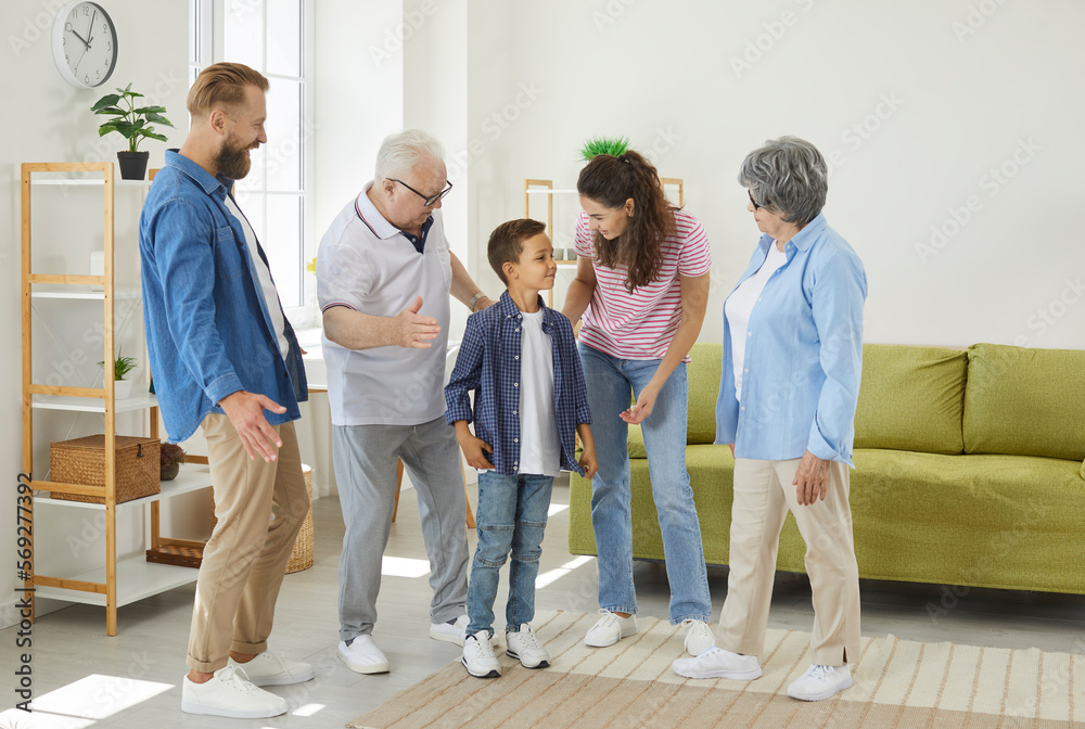 Fototapeta premium Family, happiness, generation, home and people. Happy little boy is having fun talking to his cheerful parents and grandparents. Large multigenerational family meets together at home in living room.