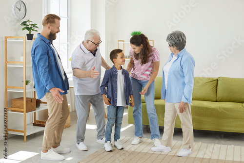 Family, happiness, generation, home and people. Happy little boy is having fun talking to his cheerful parents and grandparents. Large multigenerational family meets together at home in living room.