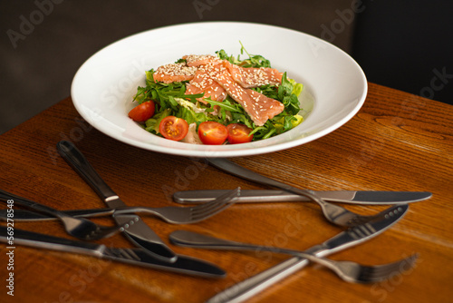 White ceramic plate of fresh salad with salmon, vegetables, tomatoes and arugula with sesame seeds. (ID: 569278548)