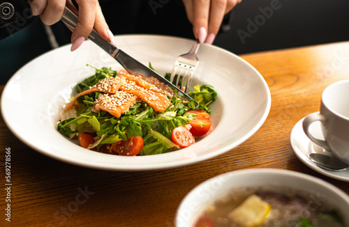 White ceramic plate of fresh salad with salmon, vegetables, tomatoes and arugula with sesame seeds.