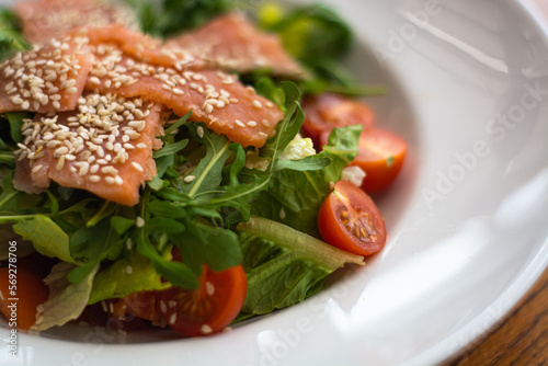 White ceramic plate of fresh salad with salmon, vegetables, tomatoes and arugula with sesame seeds. (ID: 569278706)