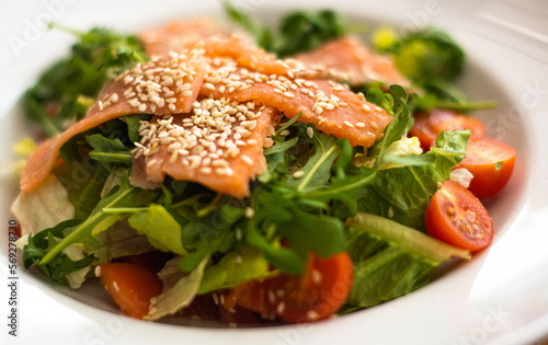 White ceramic plate of fresh salad with salmon, vegetables, tomatoes and arugula with sesame seeds. (ID: 569278730)