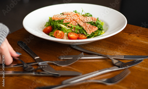 White ceramic plate of fresh salad with salmon, vegetables, tomatoes and arugula with sesame seeds. (ID: 569278743)