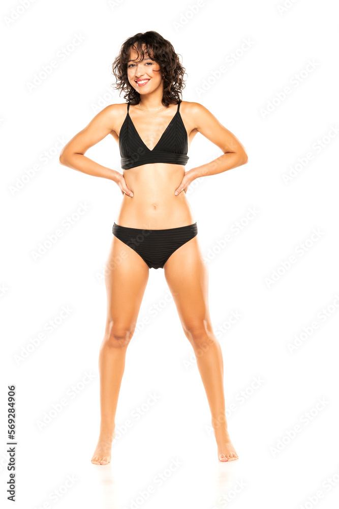 Young smiling exotic brunette woman in black bikini swimsuit posing on a white background. Front view.