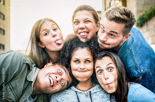 Multicultural milenial people taking selfie sticking out tongue with funny faces - Crazy life style and integration concept with interracial young friends having fun together - Vivid backlight filter