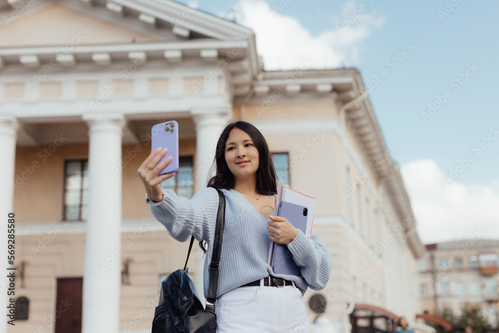 Fototapeta premium Portrait of thai student girl taking a self portrait with smart phone. Modern millennial youth lifestyle and travel concept.