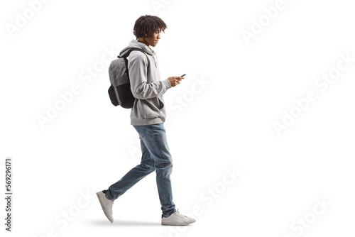 Full length profile shot of an african american male with a backpack walking and using a mobile phone