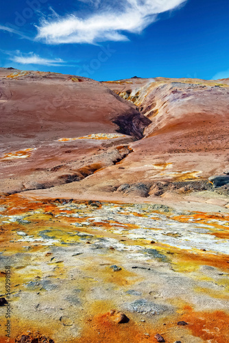 Beautiful volcanic icelandic landscape, yellow, orange and white geothermal field with sulfur deposits, fissure in red stone, blue summer sky - Seltun Krysuvik Iceland