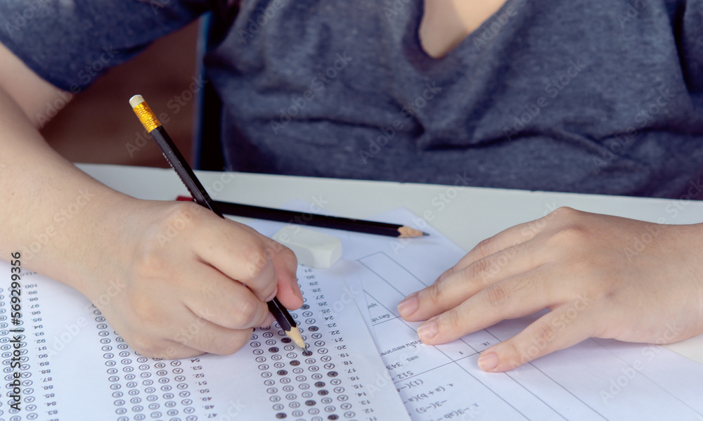 Students hand holding pencil writing selected choice on answer sheets and Mathematics question sheets. students testing doing examination. school exam Students hand holding pencil writing selected choice on answer sheets and Mathematics question sheets. students testing doing examination. school exam