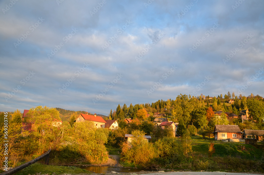 Naklejka premium Picturesque sunny autumn scenery of rolling countryside with rural houses of a small village on green and yellow hills. Slavske, Carpathian Mountains, Ukraine 