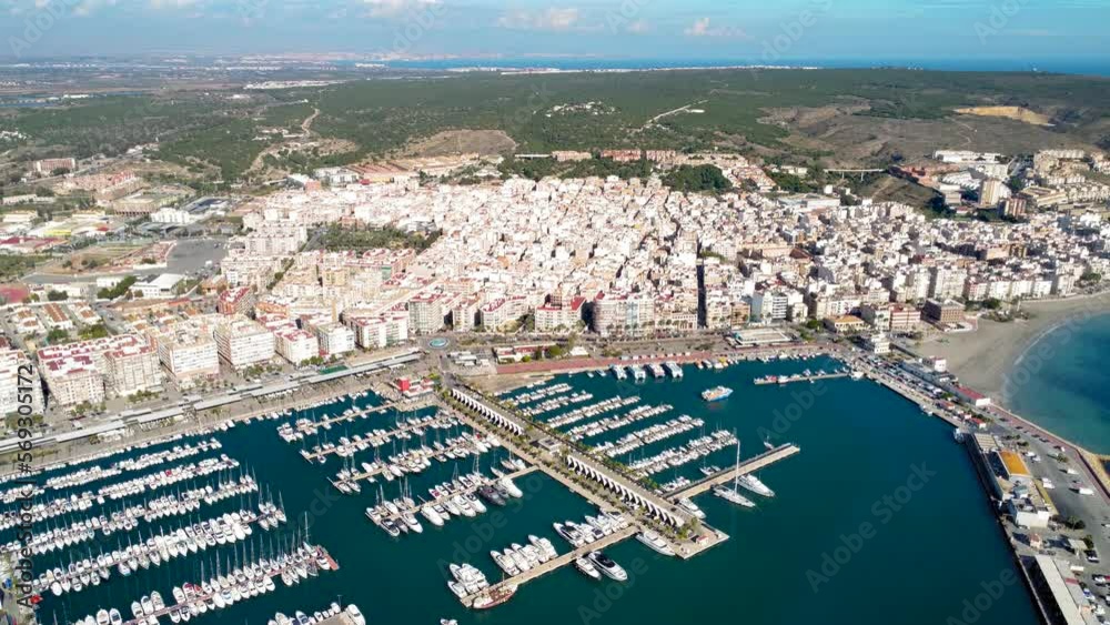 Drone point of view of Santa Pola city. View of the Marina of Santa Pola and the city center. Drone still above thee marina. Yachts docked, car passing on main boulevard. Travel destination in Spain