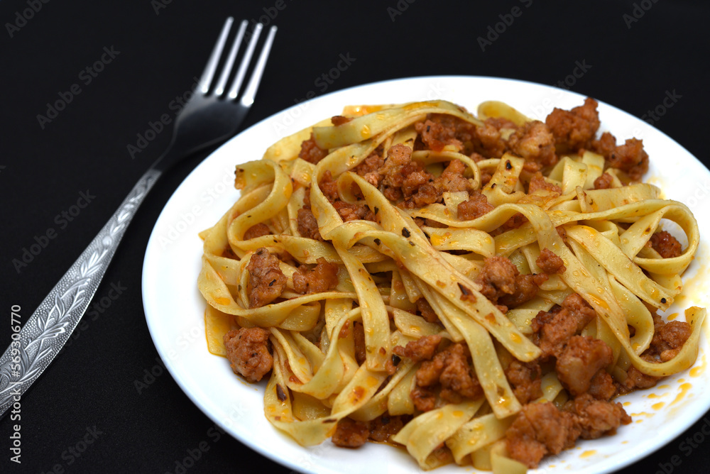 Italian pasta on a white plate with a fork. A plate of vermicelli with meat on a black background. Italian pasta on a white plate with a fork. A plate of vermicelli with meat on a black background.