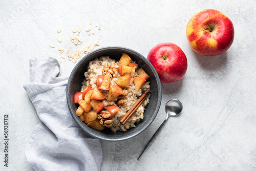 Oatmeal porrdige with apples, cinnamon and walnuts in a bowl on grey concrete table background, top view