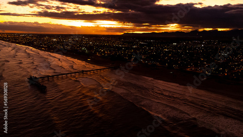 sunset on the beach besides a city with a platform over the sea