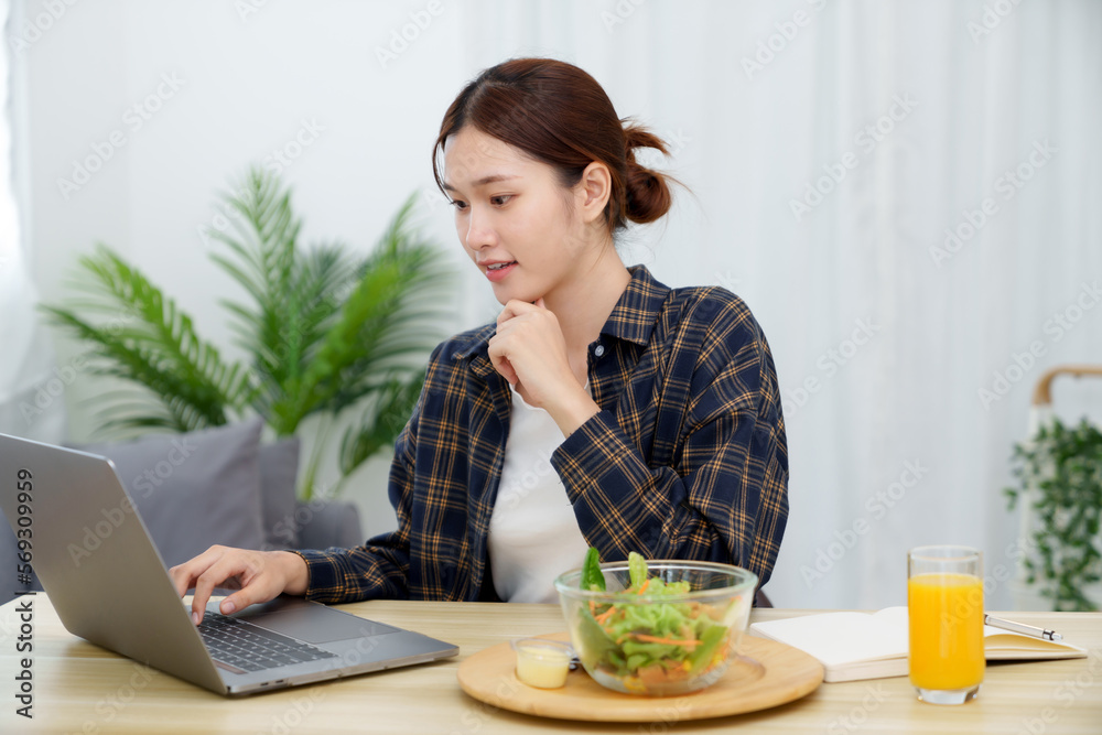 Asian businesswoman having lunch break and typing on the laptop. working at home concept Asian businesswoman having lunch break and typing on the laptop. working at home concept