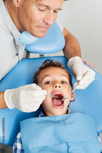  dentist examining teeth of boy. dentist in gloves using tooth on teeth of little patient while cute boy looking at camera during checkup procedure