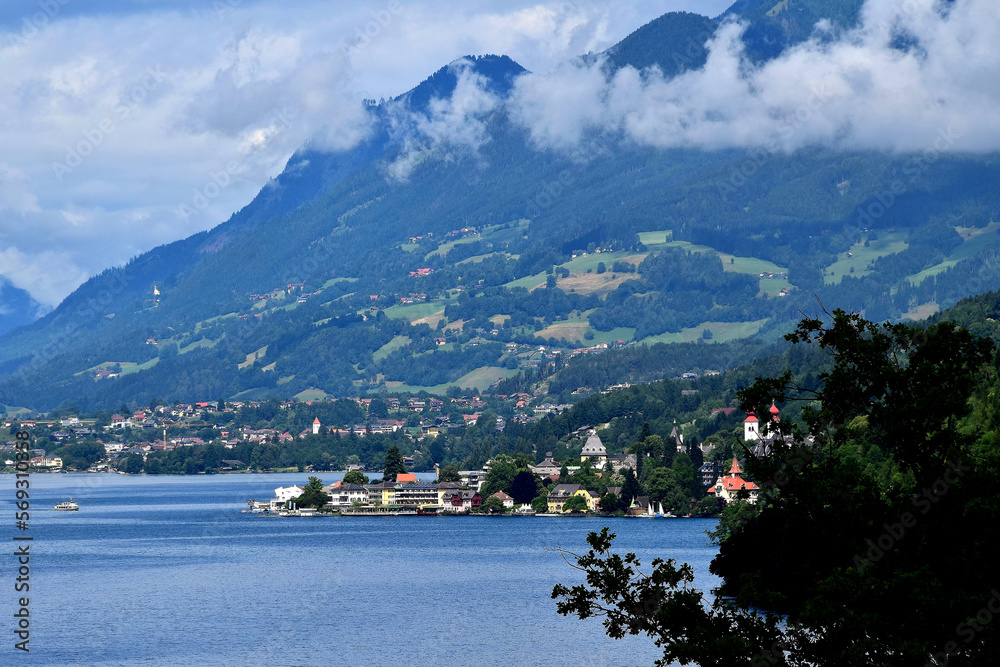 Fototapeta premium Blick auf den Millstätter See mit Millstatt und den wolkenverhangenen Nockbergen in Kärnten