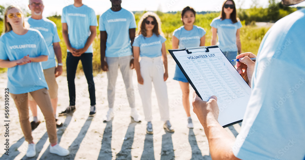 Obraz premium Close up of a clipboard with the volunteer list. The leader dividing responsibilities and checking the presence of members, participants. Nature and environment conservation concept. Save ecology.