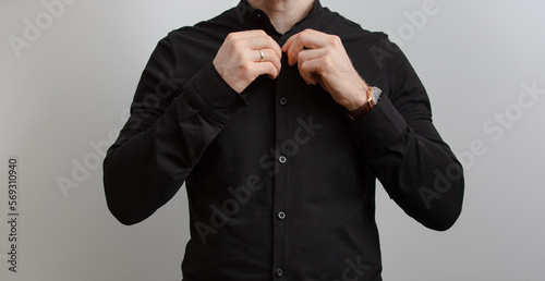 Unrecognizable man in black shirt fasten button at grey background