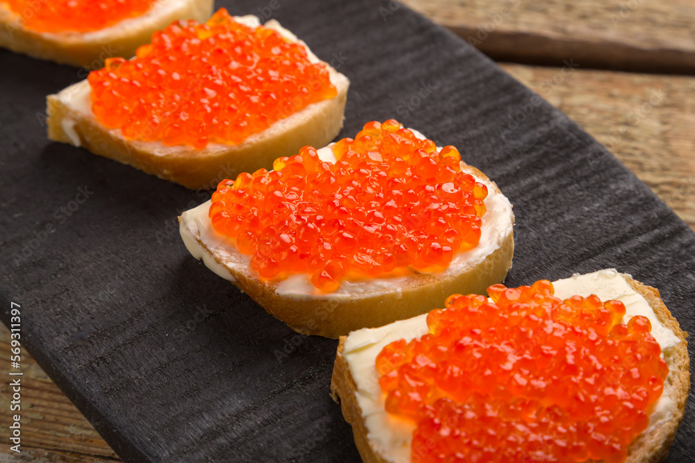 Toasts with red caviar and butter on a black board on a wooden table Toasts with red caviar and butter on a black board on a wooden table