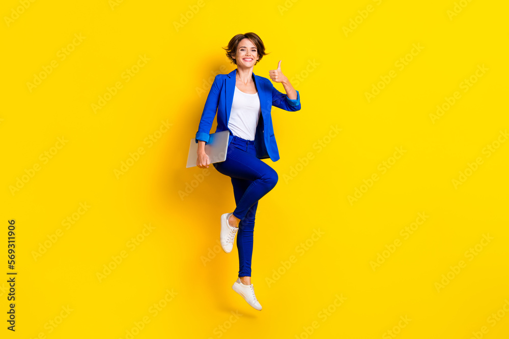 Full length photo of positive confident lady dressed blue blazer jumping thumb up holding gadget isolated yellow color background