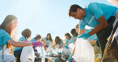 A voluntary group of different ages with the trash bags cleaning up the water. The environment activists in the gloves picking up plastic bottles, waste. Biosphere, ecological problem of pollution.