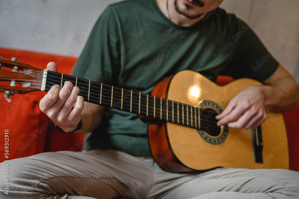 Fototapeta premium One man adult Caucasian sit at home on sofa bed in room play guitar