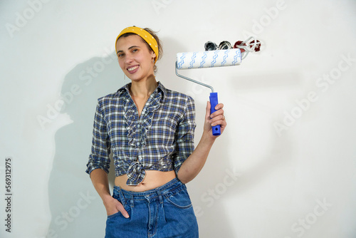 Positive overjoyed woman painter holding roller painter painting walls in room. People renovation and home improvement concept 
