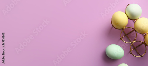 Holder with painted Easter eggs on lilac background with space for text