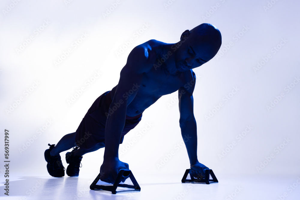 Obraz premium Athletic man is doing push ups while using special handles on studio background