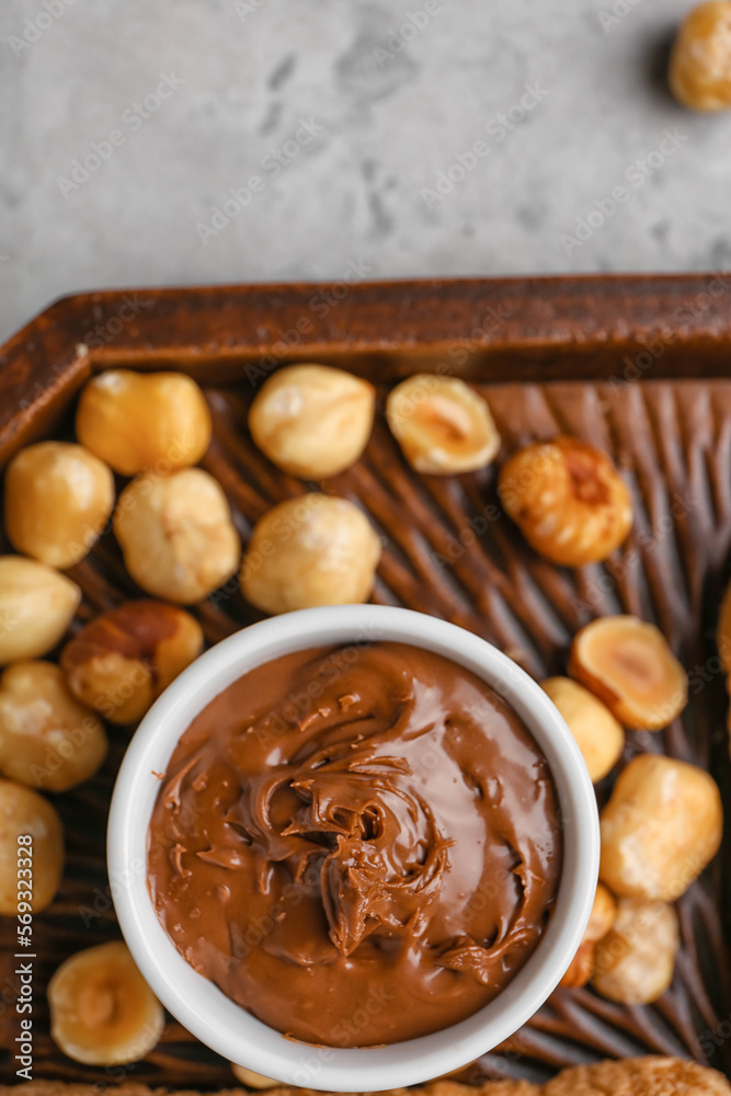 Wooden board with bowl of tasty hazelnut butter and nuts on light background, closeup Wooden board with bowl of tasty hazelnut butter and nuts on light background, closeup