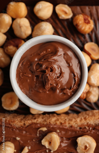 Wooden board with bowl of tasty hazelnut butter and nuts, closeup