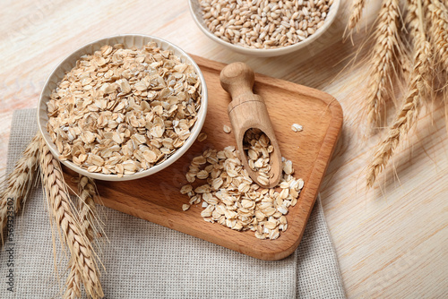 Board with bowl of raw oatmeal and spikelets on wooden background