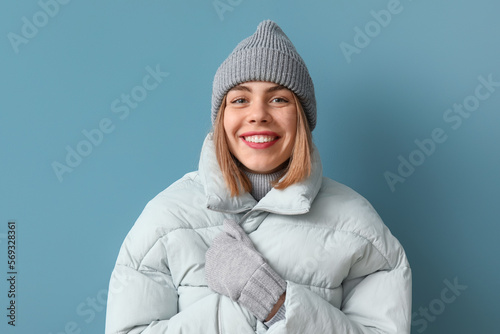 Frozen young woman in winter clothes on blue background
