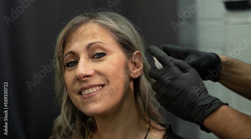 Beautiful woman in a piercing and tattoo studio. Her ear is disinfected in preparation for a piercing. Second youth concept
