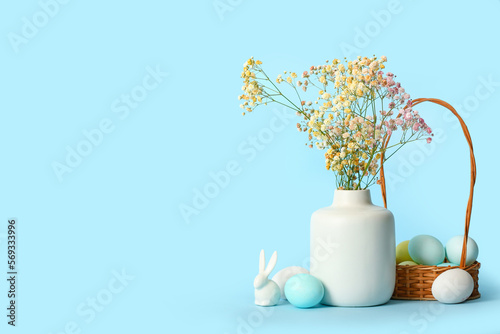 Fototapeta Naklejka Na Ścianę i Meble -  Vase with gypsophila flowers, basket of Easter eggs and bunny on color background