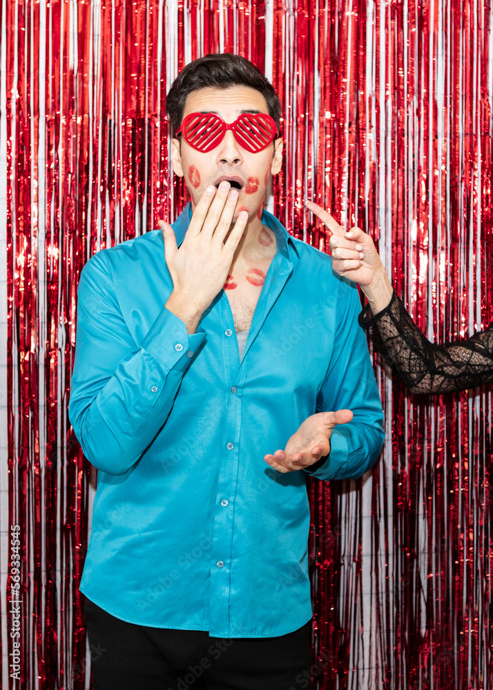 Shocked young handsome husband with many kiss marks standing in front of festive wall and