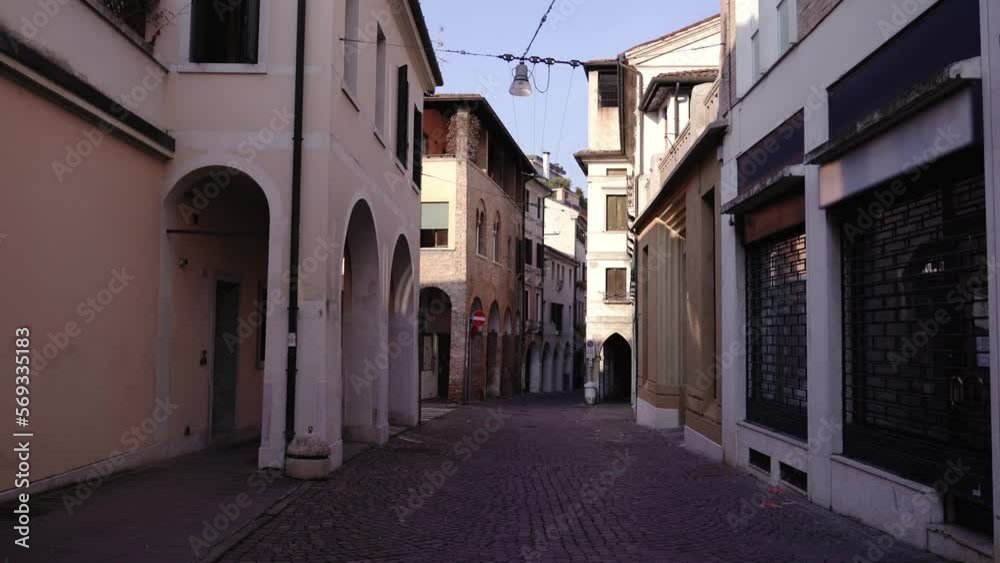 Old and new city buildings with arches surround narrow shady road with grey stone pavement and bright sunlight on open houses Old and new city buildings with arches surround narrow shady road with grey stone pavement and bright sunlight on open houses