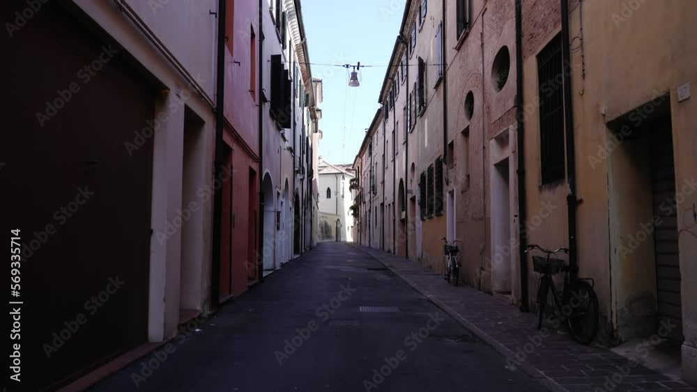 Empty narrow local street in shadow with bicycles on sidewalk locked by old brown and red buildings under blue sky at lockdown