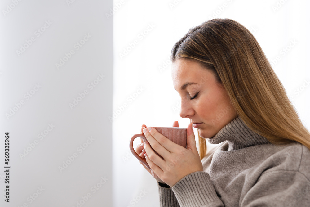 Closeup side view of pretty woman smelling cup of hot drink as coffee or tea with copy space Closeup side view of pretty woman smelling cup of hot drink as coffee or tea with copy space