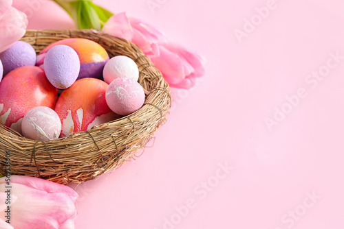 Nest with beautiful Easter eggs and tulip flowers on pink background