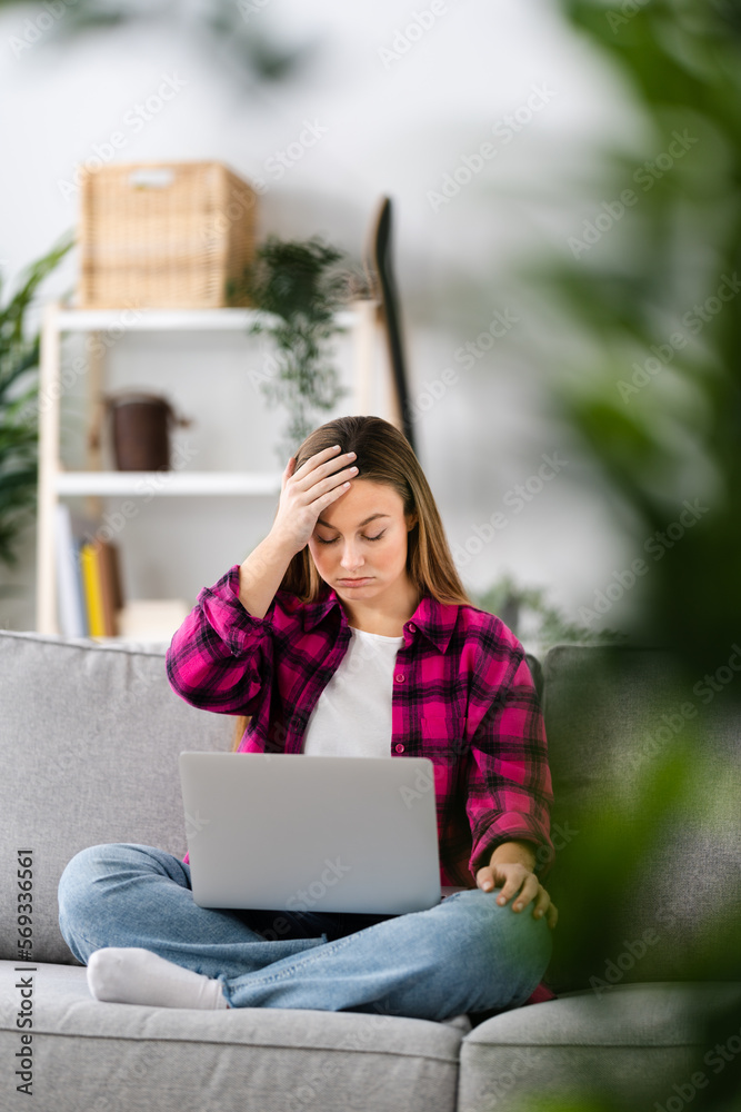 Fototapeta premium Despaired sad woman hand on head looking at laptop at home