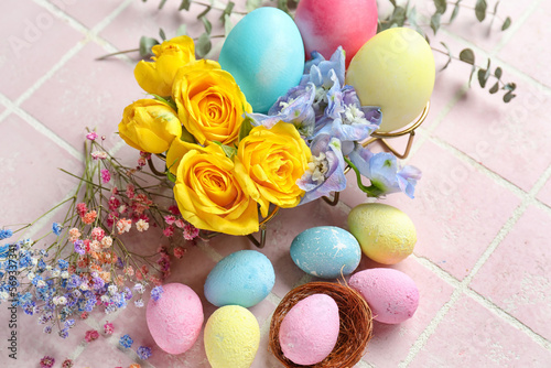 Composition with painted Easter eggs and beautiful flowers on color tile background, closeup