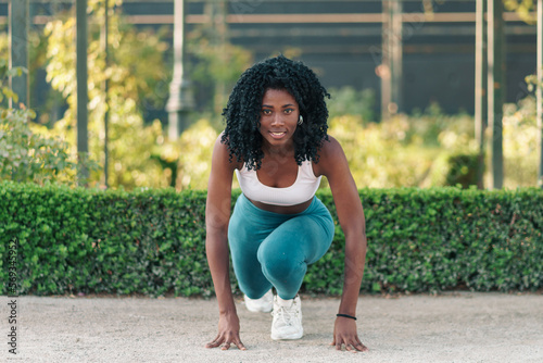 retrato de mujer negra con ropa deportiva, preparándose para hacer ejercicios, sonriendo y motivada en un parque con luz natural.	 photo